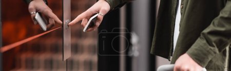 Photo pour Cropped view of man holding mobile phone and pressing call button of elevator in hotel, banner - image libre de droit