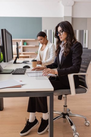 Téléchargez les photos : Interracial businesswomen in formal wear working with documents and computers in office - en image libre de droit