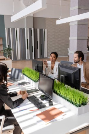 multiracial businesswoman talking to colleagues near computer monitors in modern office