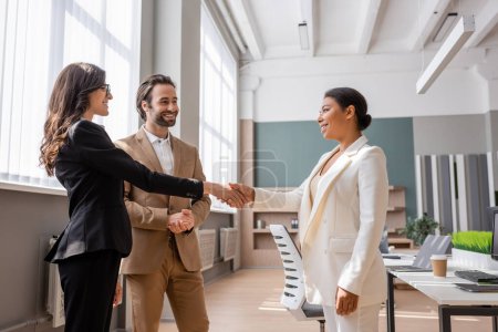 Téléchargez les photos : Young and smiling manager looking at interracial businesswomen shaking hands in office - en image libre de droit
