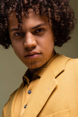 retrato del hombre afroamericano rizado en chaqueta amarilla mirando a la cámara aislada en gris