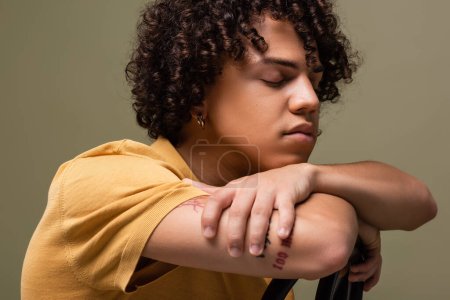 Téléchargez les photos : Stylish african american man with closed eyes and wavy hair leaning on chair back isolated on grey - en image libre de droit