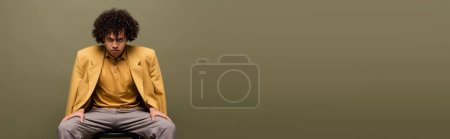 Photo for Fashionable african american man in yellow jacket and trousers looking at camera while sitting isolated on grey, banner - Royalty Free Image