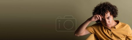 Foto de Joven afroamericano hombre con el pelo rizado morena sosteniendo la mano cerca de la cabeza y mirando a la cámara sobre fondo gris, pancarta - Imagen libre de derechos