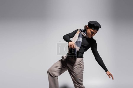 trendy african american man in black beret and plaid scarf posing on grey background