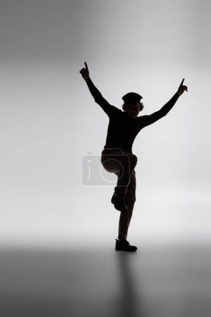 dark silhouette of african american man posing with raised hands and pointing with fingers on grey background