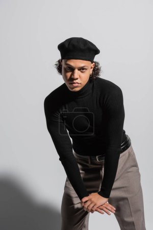 young and fashionable african american man in black beret and turtleneck looking at camera on grey background