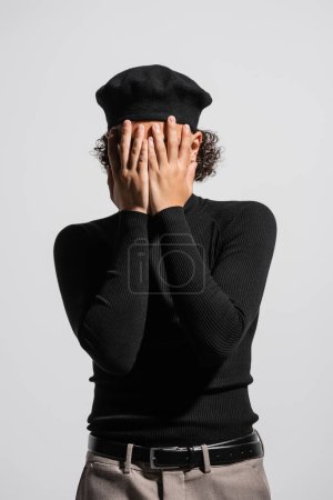 Téléchargez les photos : Young african american man in stylish beret and black turtleneck covering face with hands isolated on grey - en image libre de droit