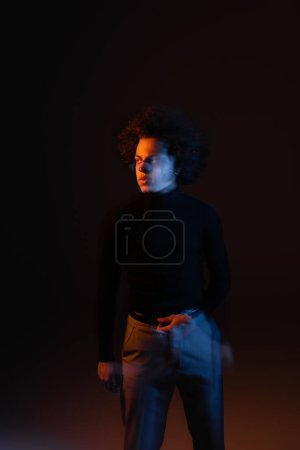 long exposure of injured african american man with bipolar disorder looking away on dark background with orange and blue light