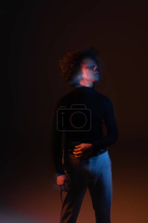 motion blur of african american man with bipolar disorder and injured face standing on dark background with orange and blue light