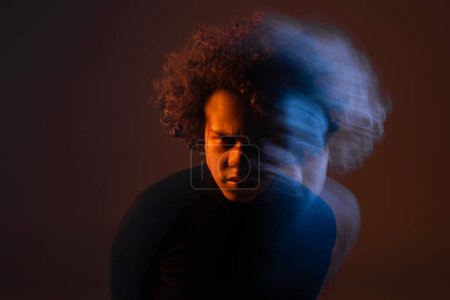 larga exposición del hombre afroamericano herido con trastorno bipolar mirando a la cámara sobre fondo oscuro con luz naranja y azul