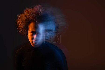 Langzeitbelichtung eines gestressten afrikanisch-amerikanischen Mannes mit bipolarer Störung und blutendem Gesicht auf dunklem Hintergrund mit orangefarbenem und blauem Licht