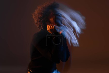 Foto de Desenfoque de movimiento del joven afroamericano con trastorno bipolar sobre fondo oscuro con luz naranja y azul - Imagen libre de derechos