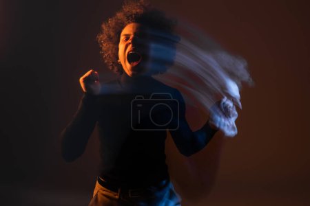 motion blur of african american man with bipolar disorder and injured face screaming with closed eyes on dark background with orange and blue light