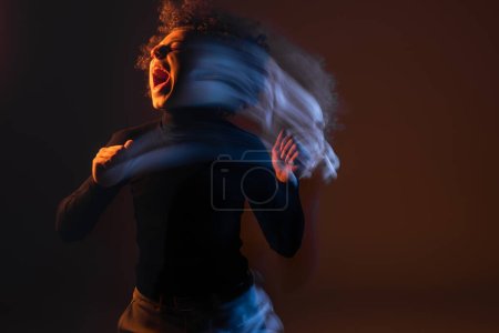 Foto de Larga exposición del hombre afroamericano lesionado y estresado gritando sobre fondo negro con luz naranja y azul - Imagen libre de derechos