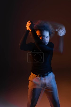 Foto de Larga exposición del hombre afroamericano herido con trastorno bipolar sobre fondo oscuro con luz naranja y azul - Imagen libre de derechos