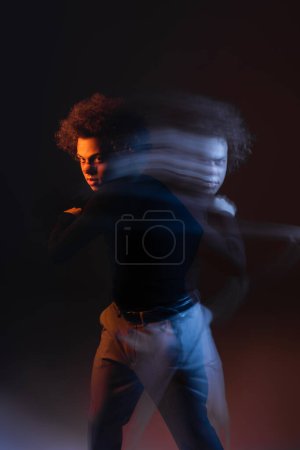 Langzeitbelichtung eines jungen und verletzten afrikanisch-amerikanischen Mannes mit bipolarer Störung, der die Kamera auf schwarz mit orangefarbenem und blauem Licht betrachtet