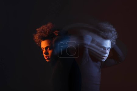 Doppelbelichtung eines verletzten afrikanisch-amerikanischen Mannes mit bipolarer Störung beim Anblick einer Kamera auf dunklem Hintergrund mit orangefarbenem und blauem Licht