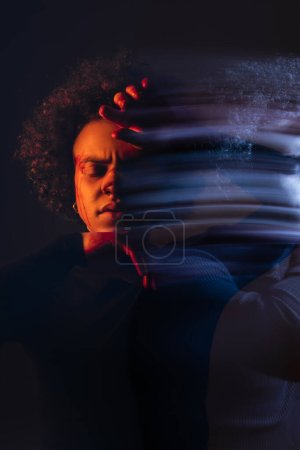 Foto de Doble exposición del hombre afroamericano deprimido con trastorno bipolar y cara sangrante lesionada sobre fondo negro con luz naranja y azul - Imagen libre de derechos