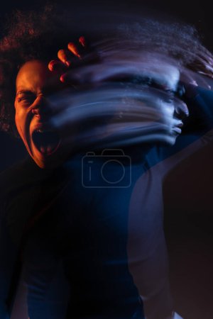 Doppelbelichtung eines irritierten afrikanisch-amerikanischen Mannes mit bipolarer Störung, der auf dunklem Hintergrund mit orangefarbenem und blauem Licht schreit