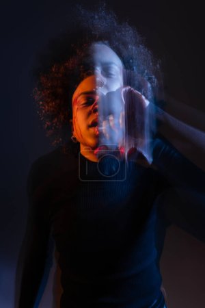 Langzeitbelichtung des verletzten afrikanisch-amerikanischen Mannes mit bipolarer Störung auf schwarz mit orangefarbenem und blauem Licht