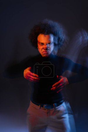 Bewegungsunschärfe eines aggressiven afrikanisch-amerikanischen Mannes mit bipolarer Störung und blutigem Gesicht, der bei Dunkelheit mit orangefarbenem und blauem Licht in die Kamera blickt