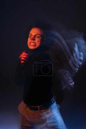 Foto de Doble exposición del hombre afroamericano abusado con trastorno bipolar y la cara sangrante mueca en la oscuridad con luz naranja y azul - Imagen libre de derechos