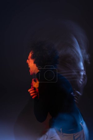 double exposure of wounded and angry african american man shouting on black background with red and blue light