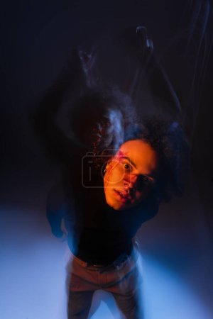 Photo for Long exposure of wounded african american man with dissociative identity disorder on black with orange and blue light - Royalty Free Image