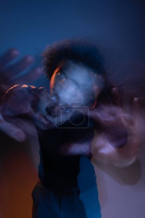 doble exposición del hombre afroamericano herido con trastorno bipolar mirando a la cámara en la oscuridad con luz naranja y azul