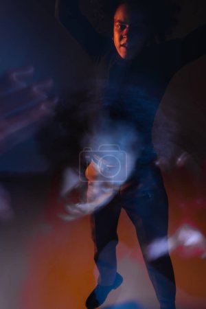 Langzeitbelichtung eines depressiven afrikanisch-amerikanischen Mannes mit bipolarer Störung und verletztem Gesicht, der im Dunkeln mit orangefarbenem und blauem Licht in die Kamera blickt