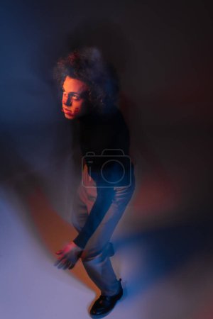 high angle view of wounded african american man with broken nose looking away on dark background with red and blue light