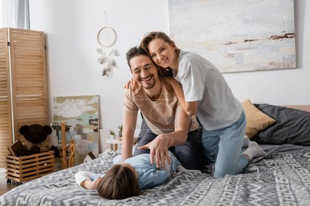 cheerful woman hugging happy husband smiling while having fun with child at home 