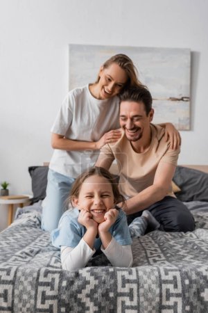 cheerful woman hugging happy husband tickling smiling daughter at home  