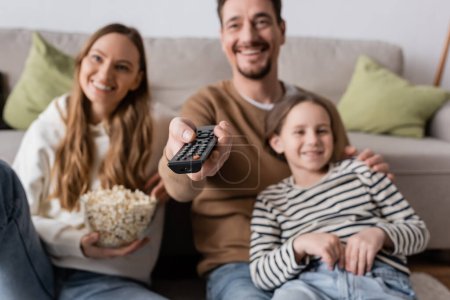 happy man holding remote controller while watching movie with family on blurred background 