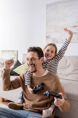 Photo for KYIV, UKRAINE - NOVEMBER 28, 2022: cheerful father and daughter holding joysticks and rejoicing after video game - Royalty Free Image