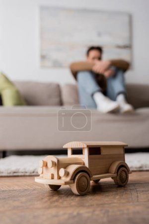 Photo for Wooden car toy near blurred man sitting on couch in living room - Royalty Free Image
