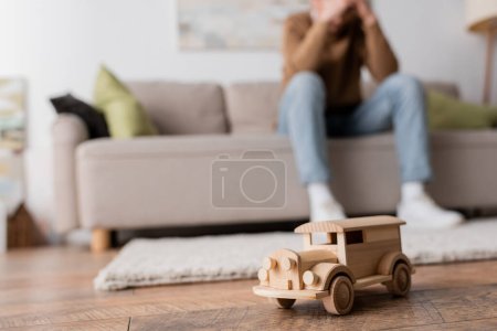 Photo for Wooden toy vehicle near cropped blurred man sitting on couch in living room - Royalty Free Image