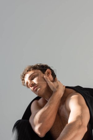 sexy shirtless man with closed eyes touching neck while posing under black blazer isolated on grey
