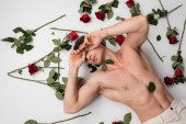 top view of shirtless muscular man with closed eyes lying near red roses on white background Stickers #634762682