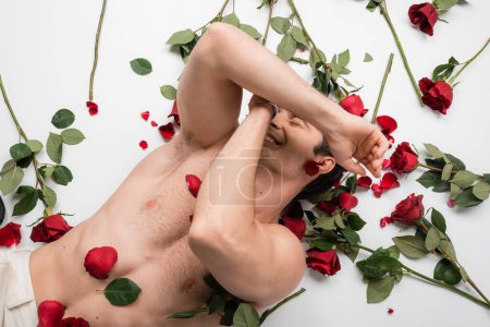 Téléchargez les photos : Top view of shirtless man with muscular torso obscuring face and smiling near red roses on white background - en image libre de droit