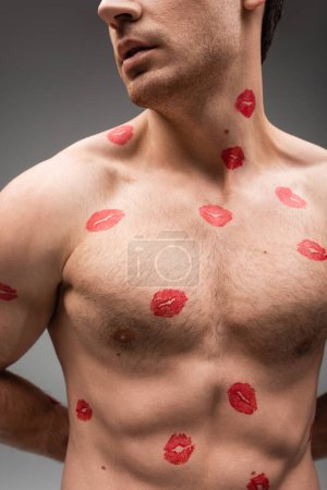 Foto de Partial view of sexy shirtless man with red lipstick marks on muscular body isolated on grey - Imagen libre de derechos