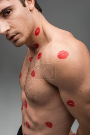Foto de Cropped view of shirtless muscular man with red kiss prints on body isolated on grey - Imagen libre de derechos