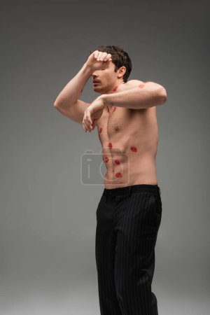 Photo for Man in black pants with red lip prints on shirtless torso obscuring face while posing on grey background - Royalty Free Image
