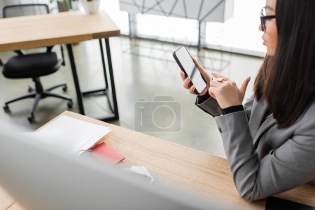 Foto de Side view of asian interior designer using smartphone near working table in office - Imagen libre de derechos
