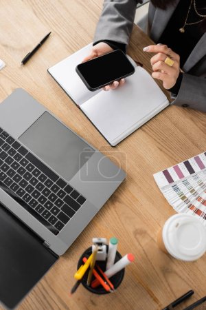 Top view of designer using smartphone with blank screen near color swatches and coffee in office 