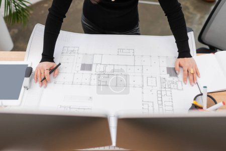 Cropped view of interior designer working with blueprint near devices in office 