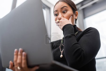 Photo for Low angle view of shocked asian interior designer holding laptop in studio - Royalty Free Image