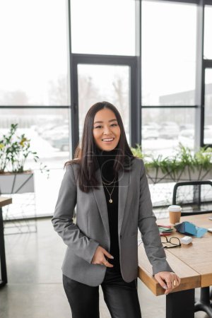 Positive asian designer looking at camera near working table in design studio 