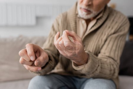 Foto de Partial view of aged man with parkinson disease and trembling hands sitting at home - Imagen libre de derechos